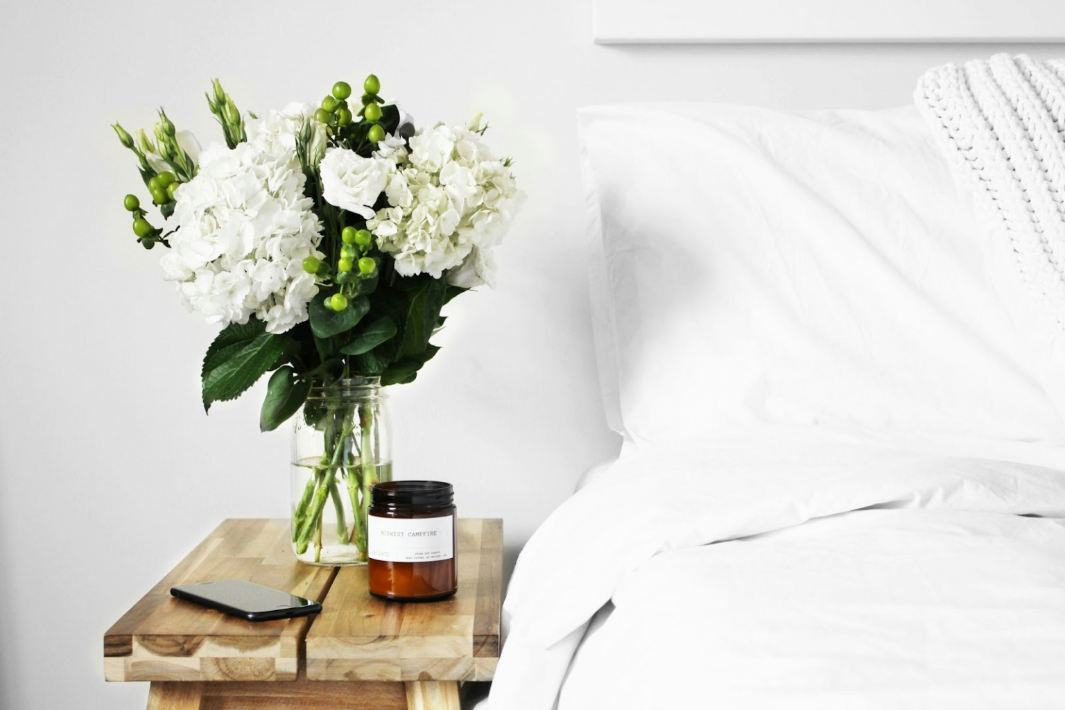 fehér ágyneművel vetett ágy, mellett fehér virágok